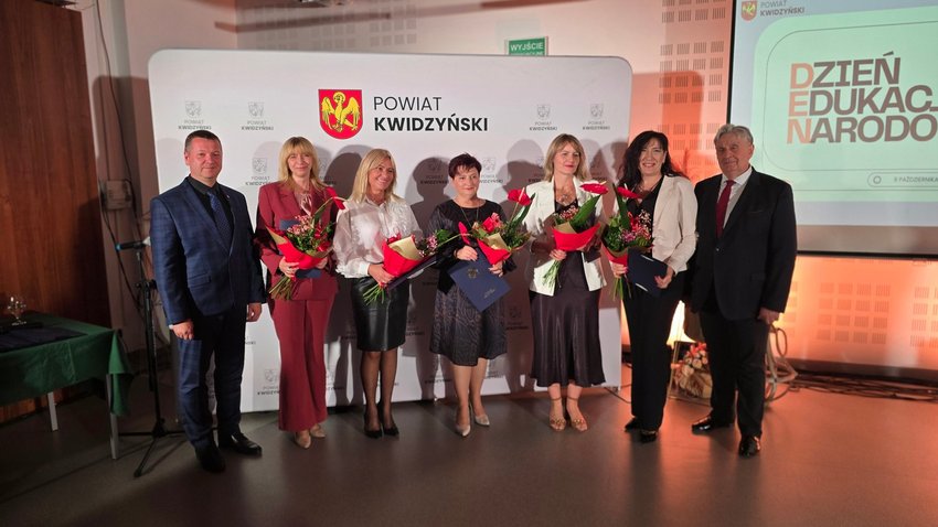  Na zdjęciu widać 5 nagrodzonych kobiet z kwiatami i listami gratulacyjnymi w towarzystwie dwóch mężczyzn, w tle ścianka Powiatu Kwidzyńskiego