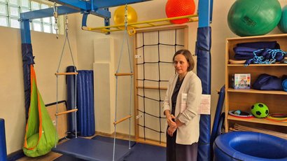 Na zdjęciu widać kobietę prezentującą salę sensoryczną – urządzenie sensoryczne z huśtawkami, materace, piłki itp.