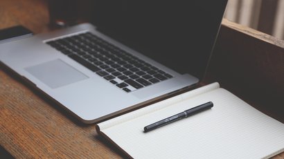 Na zdjęciu znajduje laptop oraz notes z długopisem.