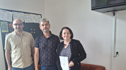 Zdjęcie przedstawia kobietę i dwóch mężczyzn stojących przed kanapą, obok tablicy z rysunkami, na ścianie wisi jedno z zamontowanych urządzeń