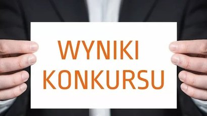 Na zdjęciu widnieją dłonie trzymające kartkę z napisem wyniki konkursu.