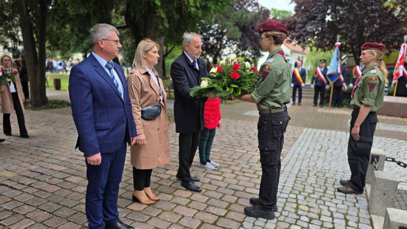 Zdjęcie przedstawia wicestarostę, który wspólnie z innymi 3 osobami przekazuje kwiaty harcerzom stojących przy pomniku