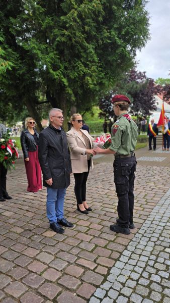 Zdjęcie przedstawia wójta i sekretarza gminy Gardeja przekazujących kwiaty harcerzowi