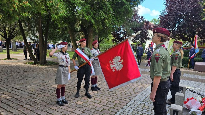 Zdjęcie przedstawia delegację 2 harcerek i harcerza ze sztandarem, stoją przed pomnikiem