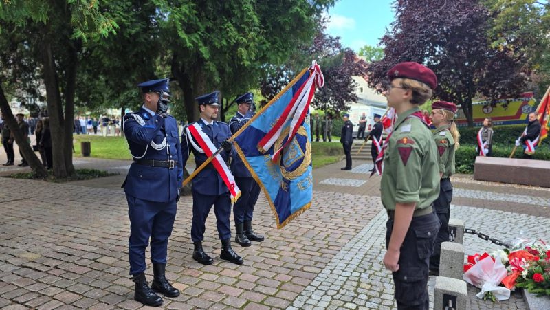 Zdjęcie przedstawia delegację  3 mężczyzn z Policji, ze sztandarem, stoją przed pomnikiem