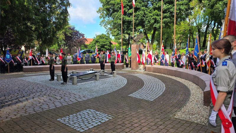 Zdjęcie przedstawia czterech harcerzy stojących przy pomniku, w tle delegacje pocztów sztandarowych