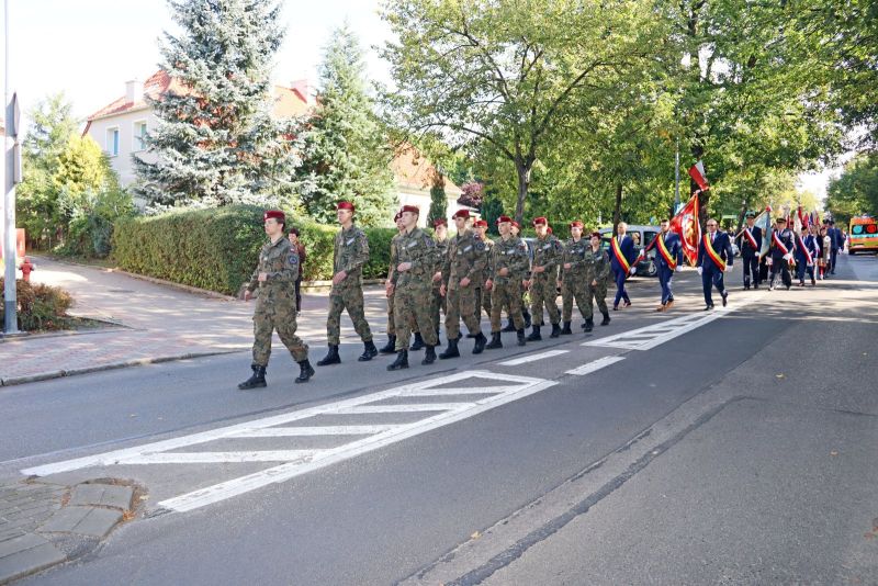 Zdjęcie przedstawia maszerujących ulicą, na pierwszym planie umundurowani uczniowie z liceum mundurowego, za nimi delegacje ze sztandarami