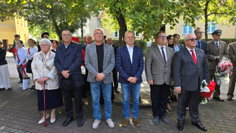 Zdjęcie przedstawia grupę zaproszonych gości stojących na chodniku, na pierwszym planie 5 mężczyzn i jedna kobieta