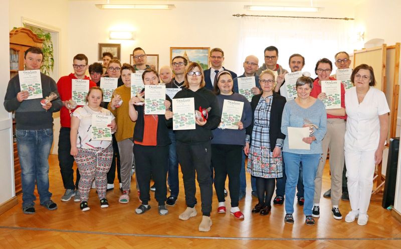 Zdjęcie pamiątkowe uczestników Warsztatu Terapii Zajęciowej po otrzymaniu dyplomów. Wraz z nimi pozują Krzysztof Michalski, zastępca wójta gminy Kwidzyn oraz opiekunowie WTZ.