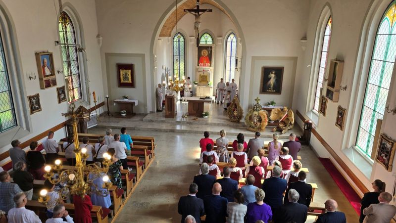 Uczestnicy mszy świętej w kościele z okazji dożynek, na pierwszym planie ołtarz ustrojony wieńcami dożynkowymi.