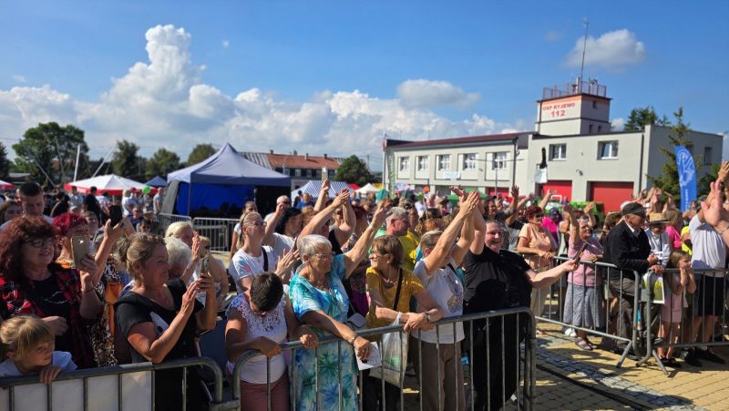 Mieszkańcy zebrali się przed sceną przy barierkach; widać, że dobrze się bawią.