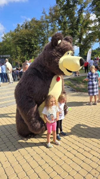 Dwie dziewczynki w wieku przedszkolnym stoją przy dużej maskotce misia.