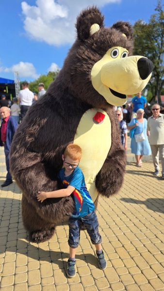 Chłopiec w wieku szkolnym przytula się do dużej maskotki misia.