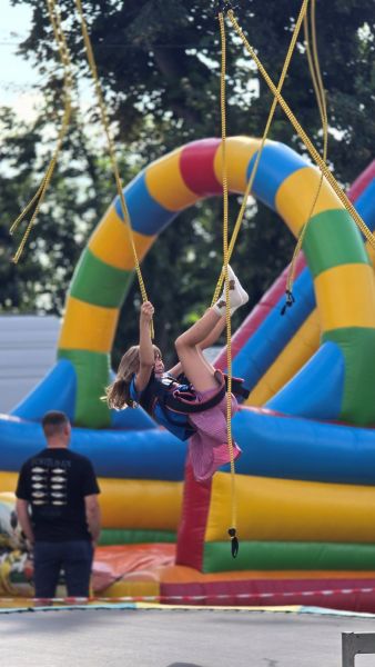 Dziewczynka w wieku szkolnym skacze na trampolinie, w tle dmuchańce do skakania.