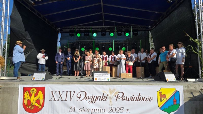  Gospodarze, zaproszeni goście oraz nagrodzone i wyróżnione osoby stoją na scenie, na pierwszym planie baner z napisem: XXIV Dożynki Powiatowe, 31 sierpnia 2025.