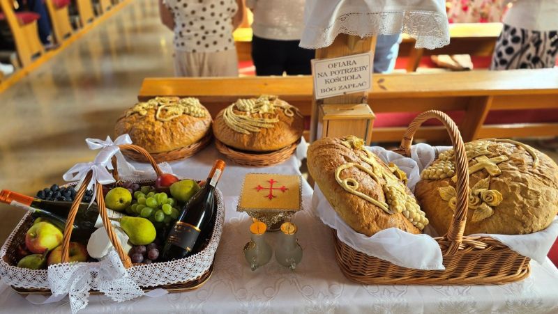 Stół w kościele, odświętnie udekorowany, na nim wiklinowe kosze z bochenkami chlebów, winem, owocami.