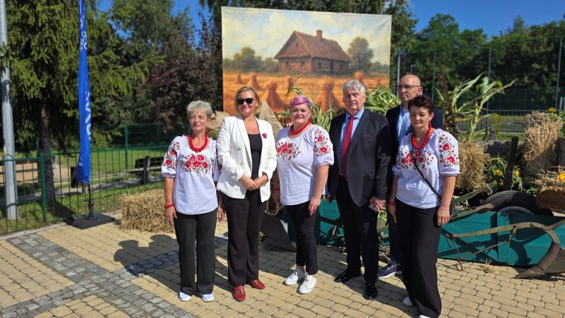 Grupa sześciu osób pozuje do zdjęcia na tle dekoracji dożynkowej.