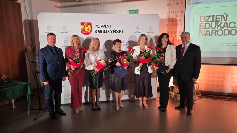 Na zdjęciu widać 5 nagrodzonych kobiet z kwiatami i listami gratulacyjnymi w towarzystwie dwóch mężczyzn, w tle ścianka Powiatu Kwidzyńskiego