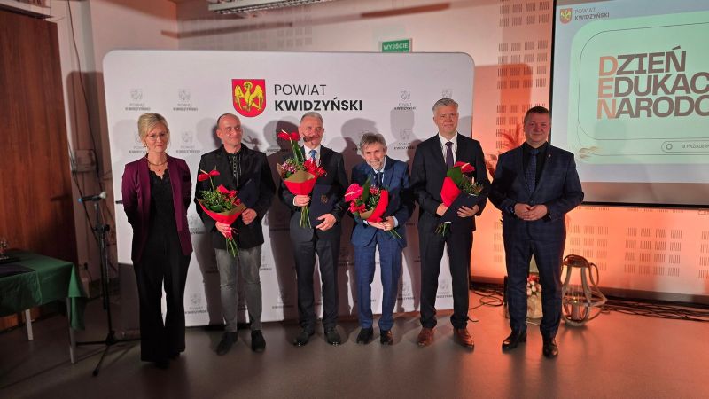 Na zdjęciu widać 4 nagrodzonych z kwiatami i listami gratulacyjnymi w towarzystwie kobiety, w tle ścianka Powiatu Kwidzyńskiego