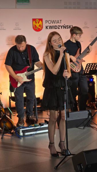 Na zdjęciu widać wokalistkę, za nią 2 gitarzystów