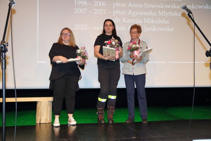 Trzy kobiety zaangażowane w działalność harcerską stoją razem na scenie podczas wręczenia wyróżnień.