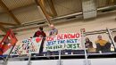 Zdjęcie przedstawia dwóch mężczyzn stojących na trybunach hali sportowej, a poniżej znajdują się dwa plakaty z napisem: Zawsze i wszędzie OSP Benowo Mistrzem będzie oraz OSP Benowo jest the best, tak było i jest. 