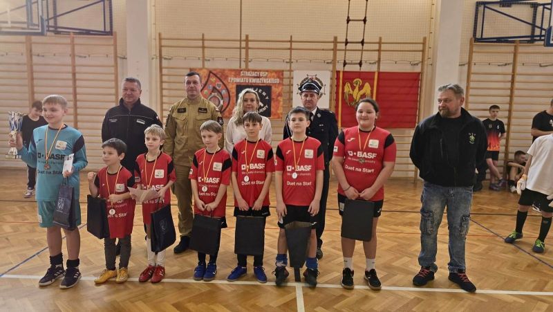 Zdjęcie przedstawia uśmiechnięte dzieci.Za nimi Tomasz Frejnagiel, Piotr Sztypka, Katarzyna Ochlik-Rafka, Tomasz Kazimierczyk oraz trener drużyny.
