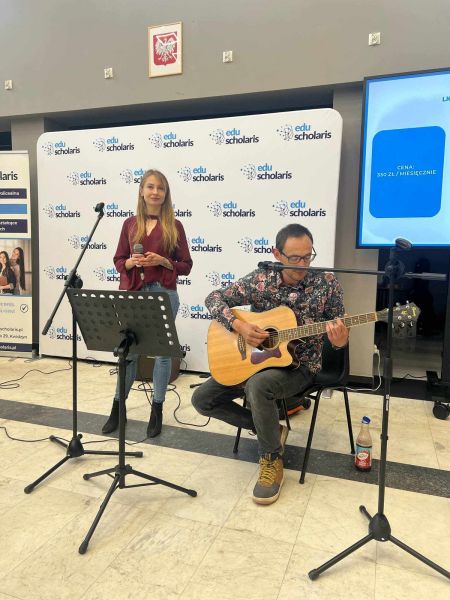 zdjęcie przedstawia kobietę i mężczyznę. Mężczyzna gra na gitarze, kobieta stoi przy mikrofonie.