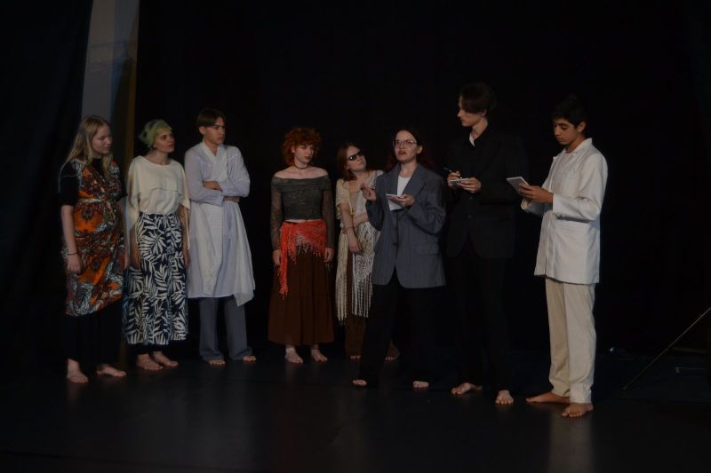 Na zdjęciu widać grupę ludzi z zaciekawionymi minami. Widać również dziewczynę, która coś opowiada.