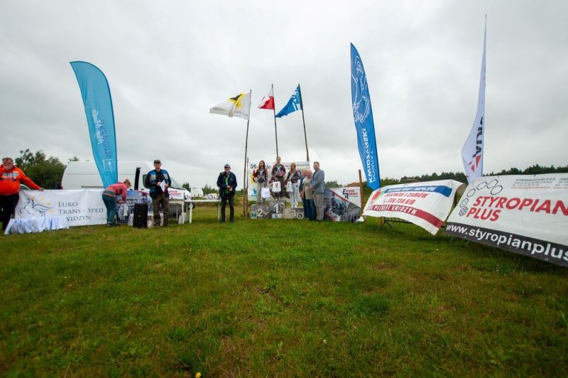 Na zdjęciu znajduje się grupa ludzi oraz trzy osoby stojące na podium.