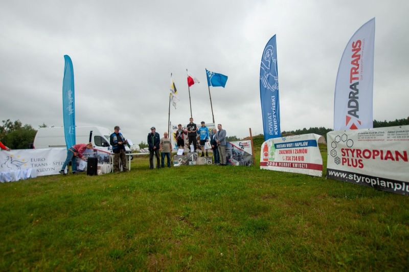 Na zdjęciu znajduje się grupa ludzi oraz trzy osoby stojące na podium.