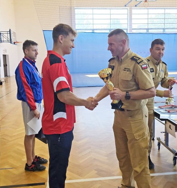 Przedstawiciel PSP, ubrany w mundur wręcza puchar mężczyźnie ubranemu na sportowo.