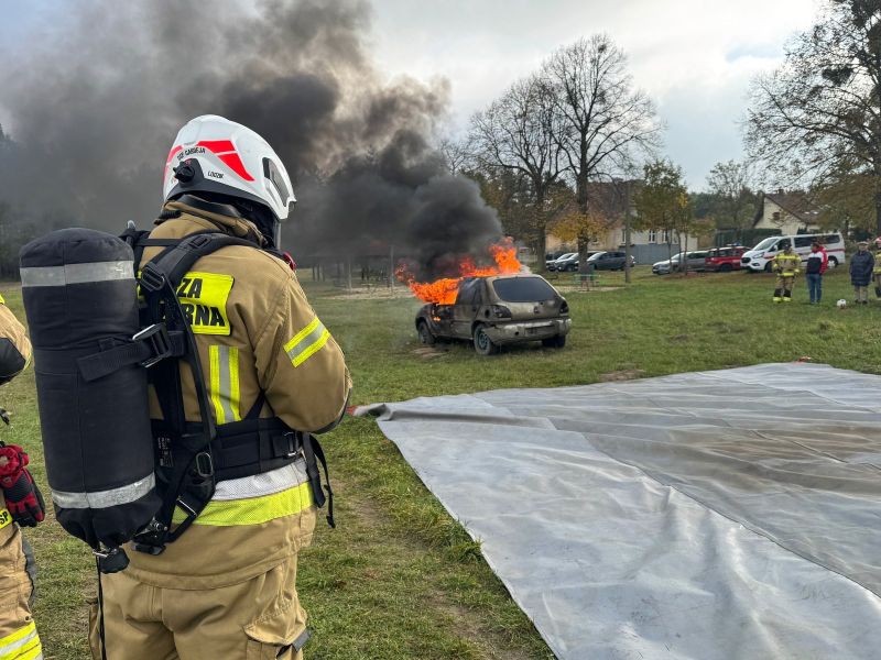 Strażacy w trakcie akcji gaśniczej płonącego pojazdu, z wykorzystaniem otrzymanej płachty gaśniczej.