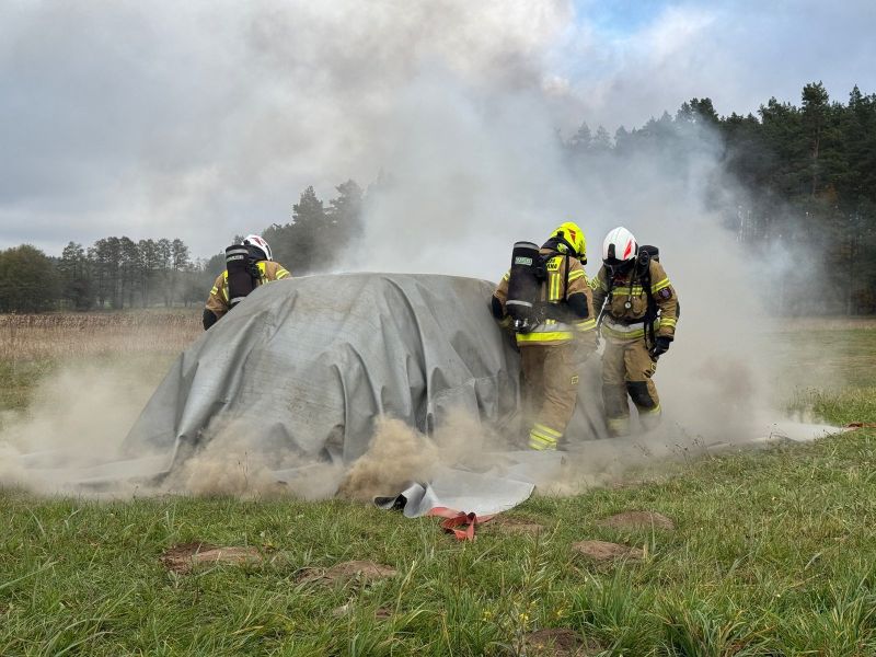 Strażacy w trakcie akcji gaśniczej płonącego pojazdu, z wykorzystaniem otrzymanej płachty gaśniczej.