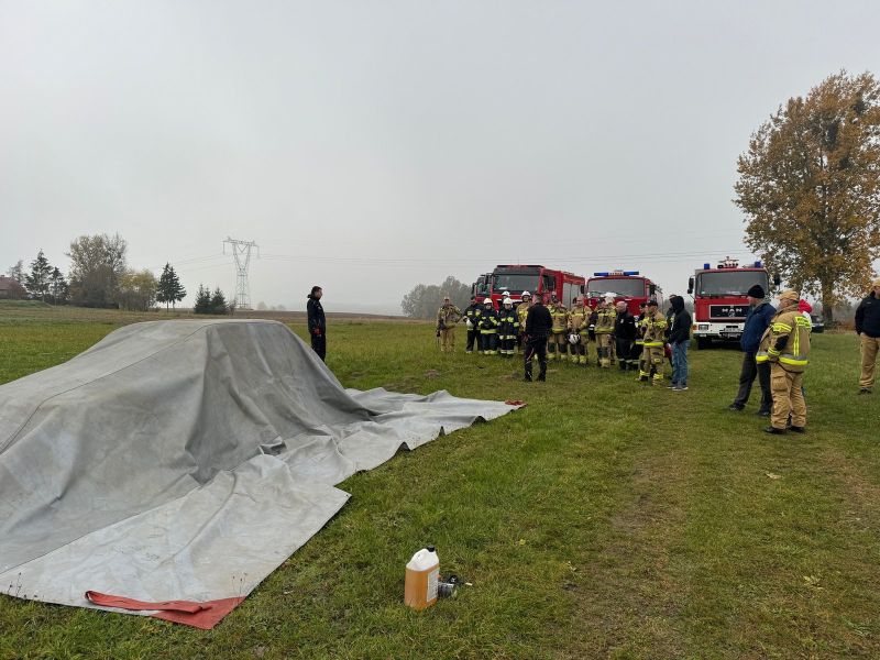 Strażacy w trakcie akcji gaśniczej płonącego pojazdu, z wykorzystaniem otrzymanej płachty gaśniczej.