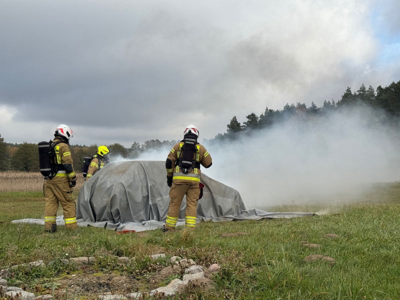 Strażacy w trakcie akcji gaśniczej płonącego pojazdu, z wykorzystaniem otrzymanej płachty gaśniczej.