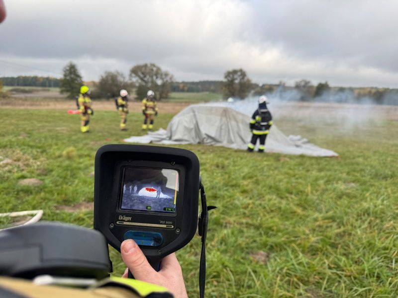 Strażacy w trakcie akcji gaśniczej płonącego pojazdu, z wykorzystaniem otrzymanej płachty gaśniczej.