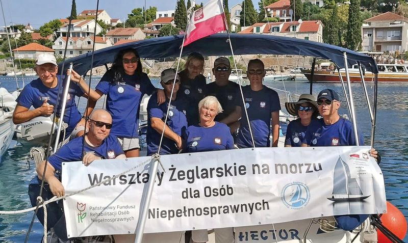 Członkowie Pomorskiego Stowarzyszenia Żeglarzy pozują do zdjęcia na łodzi.