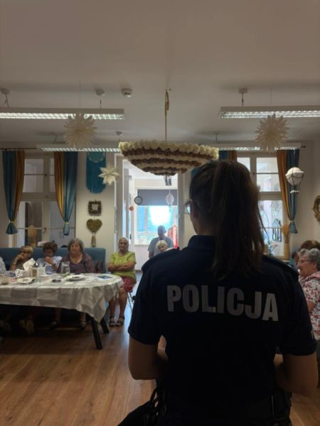 zdjęcie przedstawia policjantkę stojącą tyłem, a w tle osoby starsze. 