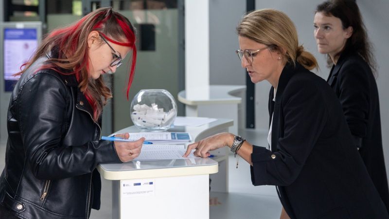 zdjęcie przedstawia trzy kobiety. Jedna instruuje drugą, gdzie podpisać dokument. 