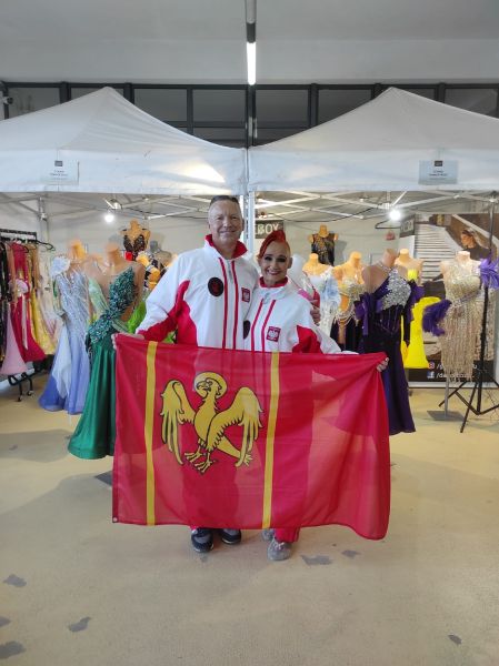 Para taneczna Monika i Mariusz Budyś w strojach reprezentacji narodowej prezentuje flagę powiatu kwidzyńskiego w kuluarach zawodów