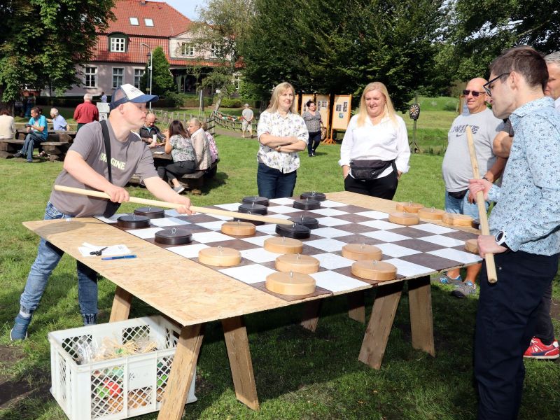 Zdjęcie przedstawia grupę ludzi podczas pikniku; na pierwszym planie widać dwóch grających w wielkie warcaby
