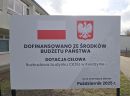 tablica informacyjna o dofinansowaniu na tle budynku szkoły.