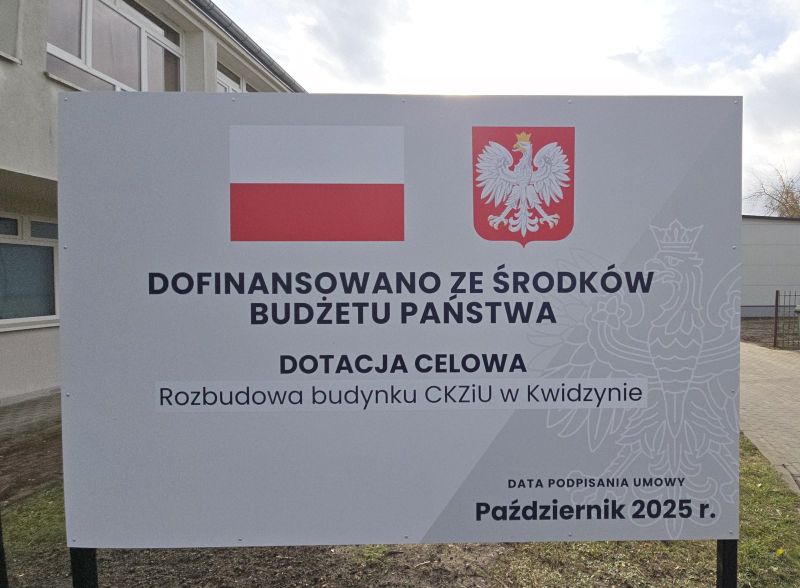 tablica informacyjna o dofinansowaniu na tle budynku szkoły.