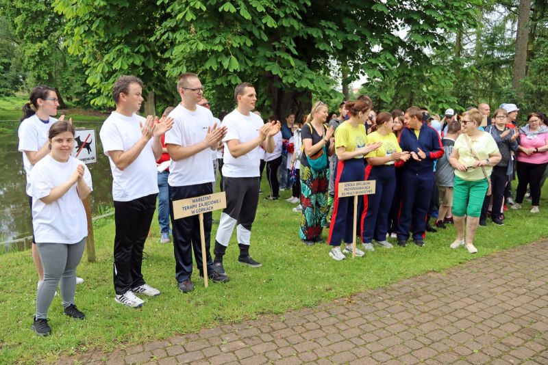 Drużyny biorące udział w spartakiadzie stoją razem na terenie parku. Uczestnicy ubrani w sportowe stroje.
