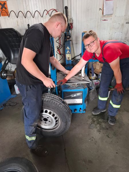 zdjęcie przedstawia stażystów podczas stażu uczniowskiego naprawiających oponę samochodową;