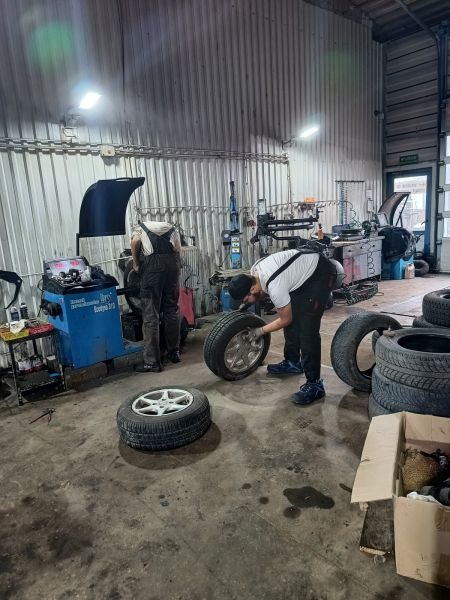 zdjęcie przedstawia stażystów podczas stażu uczniowskiego naprawiających opony samochodowe