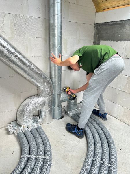 zdjęcie przedstawia stażystę podczas stażu uczniowskiego, który montuje rury w pomieszczeniu