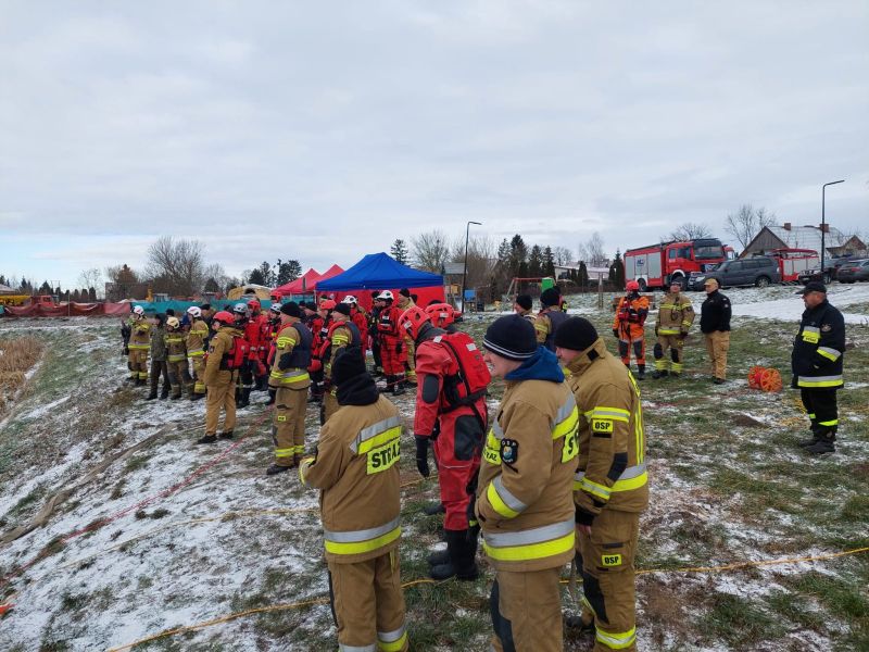 Strażacy obserwują kolegów, którzy już biorą udział w ćwiczeniach, przygotowując się do swojej kolejki w ramach symulacji ratunkowych.
