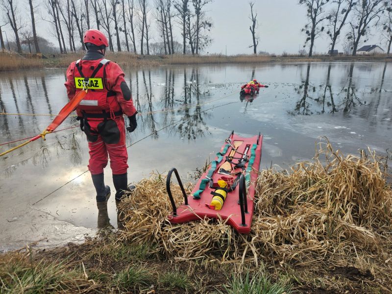 Strażacy przeprowadzają akcję ratunkową na zamarzniętym akwenie, stosując odpowiednie techniki w trudnych warunkach lodowych.